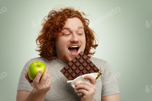Preview: Cheerful American Redhead Obese Man Opening Mouth Widely, Holding Big Bar Of Chocolate In One Hand