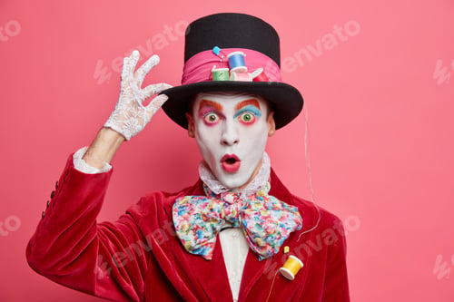 Preview: Crazy Hatter With Colorful Makeup White Face Looks Surprisingly At Camera Holds Hand On Hat Stares