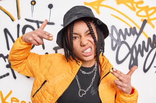 Preview: Funky Urban Teenage Girl With Dreadlocks Makes Yo Gesture Poses Against Graffiti Artwork Dressed In