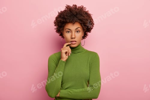 Vista previa: Horizontal Shot Of Serious Calm Dark Skinned Curly Woman Wears Round Earrings, Green Turtleneck