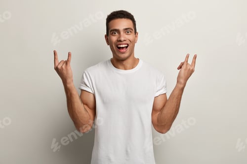 Preview: Happy Pleased Man With Cheerful Facial Expression, Makes Rock N Roll Gesture, Enjoys Cool Music