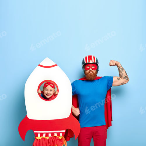 Preview: Serious Dad Shows Biceps, Dressed In Headgear, Blue T Shirt And Red Cape, Pretends Being Superhero