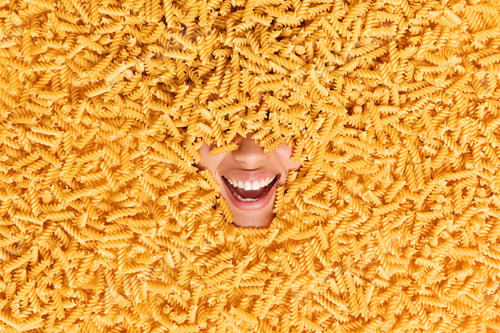 Preview: Joyful Unrecognizable Woman Buried In Uncooked Pasta Shows White Teeth Smiles Broadly Surrounded By