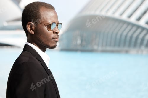 Preview: Sideview Of Smiling Stylish Dark-Skinned Banker Wearing Black Suit And Round Sunglasses Walking To