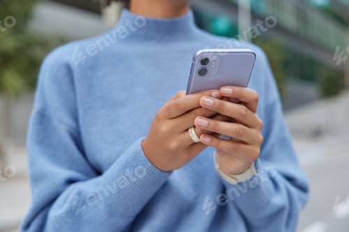 Preview: Cropped Image Of Unrecognizable Faceless Woman In Casual Blue Jumper Holds Mobile Phone Types Sms