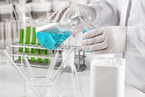 Preview: Young Clinical Worker Dressed In White Gown And Gloves Holding Glass Beakers With Blue Liquid