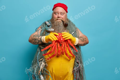 Preview: Skillful Bearded Fisherman Holds Big Octopus In Hands Caught With Fishing Net, Poses In Port, Wears
