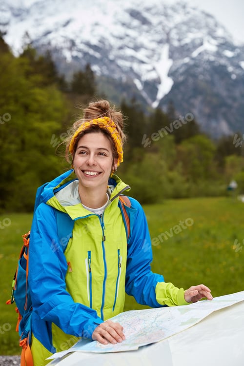 Preview: Positive Caucasian Female Traveler Stands Near Map, Studies Route, Wears Yellow Scarf On Head