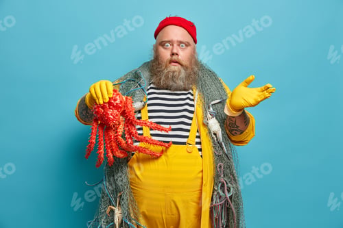 Preview: Photo Of Impressed Stout Bearded Seaman Holds Octopus And Raises Hand In Bewilderment, Wears Red
