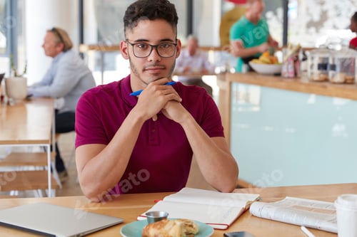 Preview: Shot Of Handsome Serious Mixed Race Young Man Writer Holds Pen, Makes List To Do In Notepad, Drinks