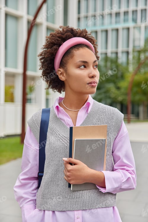 Preview: Vertical Shot Of Curly Female Student Dressed In Neat Clothes Carries Notebooks Returns From