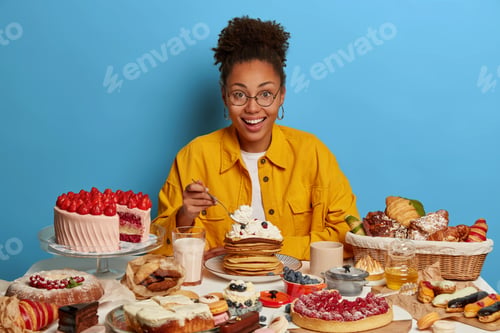Preview: Pleased Satisfied Dark Skinned Woman Eats Delicious Desserts, Holds Spoon, Enjoys Eating Cream