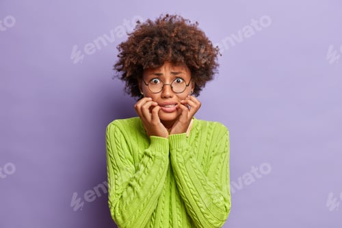 Preview: Photo Of Dark Skinned Worried Woman Bites Finger Nails And Looks Anxious At Camera Worries Before