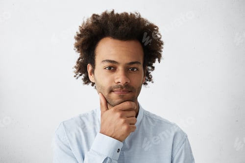 Preview: Good-Looking Dark-Skinned Male With Curly Hair Having Pensive Expression Holding Hand On Chin