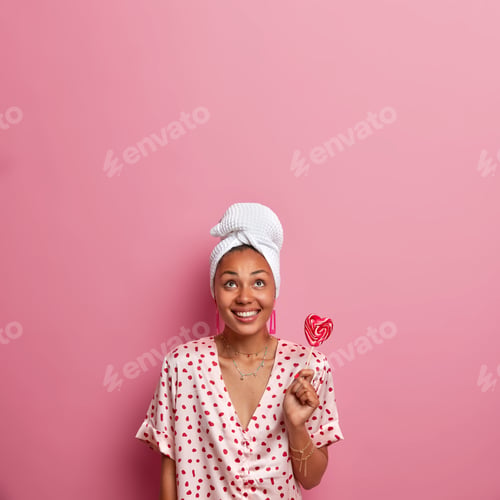 Preview: Vertical Shot Of Pleased Smiling Woman Has Dark Skin, Holds Delicious Appetizing Lollipop, Wears