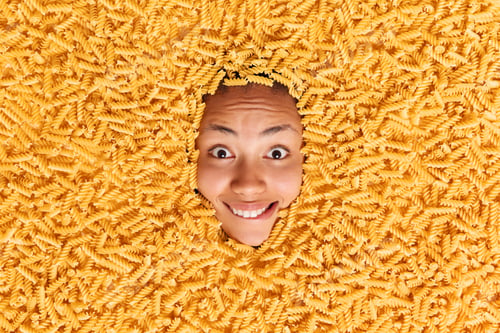 Preview: Surprised Happy Positive Young African American Woman Sticks Head Through Raw Yellow Macaroni