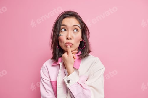 Preview: Photo Of Thoughtful Dreamy Woman With Eastern Appearance Looks Up Keeps Thumb Near Lips Makesup Her