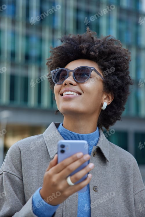 Preview: Happy Female Blogger Uses Cellphone For Finding Route Strolls In City Wears Sunglasses And Grey