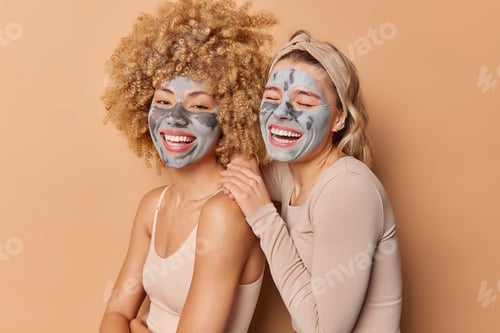 Preview: Indoor Shot Of Happy Young Pretty Women Apply Clay Masks Smile Broadly Dressed Casually Stand