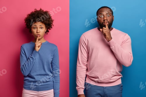 Preview: Photo Of Surprised Afro American Woman And Man Press Index Fingers On Lips, Asks Be Silent And