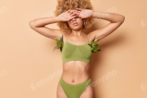 Preview: Tender Curly Woman Wears Green Bodysuit Covers Eyes With Hands Has Perfect Figure Healthy Skin Well
