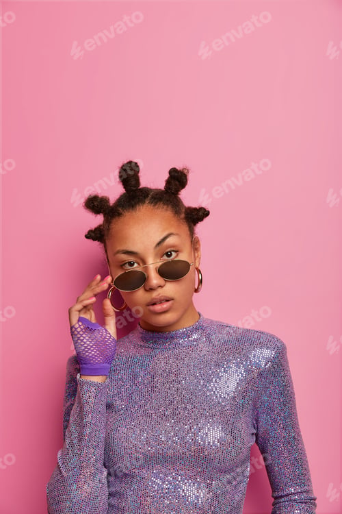Preview: Self Confident Attractive Female Has Funny Hairstyle With Buns, Keeps Hands On Shades, Wears
