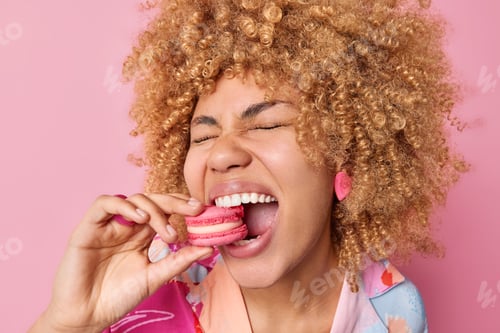Preview: Close Up Shot Of Cheerful Curly Haired Woman Keeps Mouth Widely Opened Bites Delicious Macaroon
