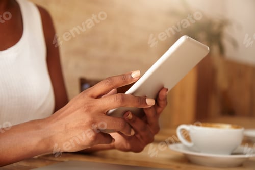 Preview: Croped Portrait Of Young Dark-Skinned Girl In White Tank Top, Sitting At The Cafe Table, Typing On