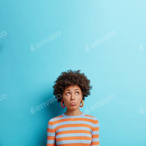 Preview: Vertical Shot Of Unhappy Dark Skinned Woman Looks With Gloomy Discontent Face Expression Upwards