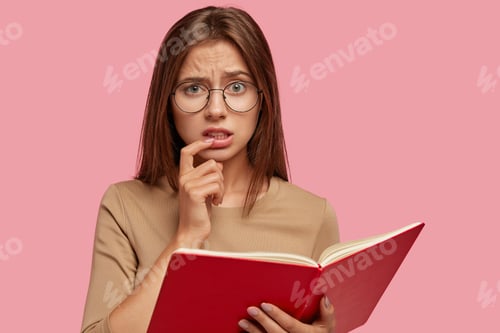 Preview: Studio Shot Of Displeased Dark Haired Woman Frowns Face, Keeps Index Finger Near Mouth, Feels