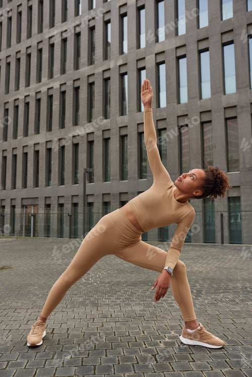 Preview: Full Length Shot Of Sporty Young African American Woman Raises Arms Exercises Outdoors Enjoys