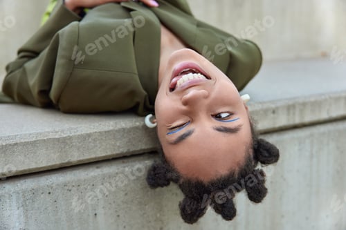 Preview: Playful Fashionable Young Woman With Hair Buns Winks Eyes Sticks Out Tongue Dressed In Green Jacket