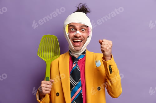Preview: Positive Funny Man With Bruises Under Eyes Bandaged Head, Clenches Fist And Giggles Positively