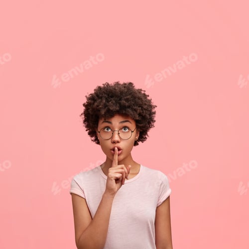 Preview: Cute Young Curly African American Female Model Makes Silence Sign, Looks Upwards At Blank Copy