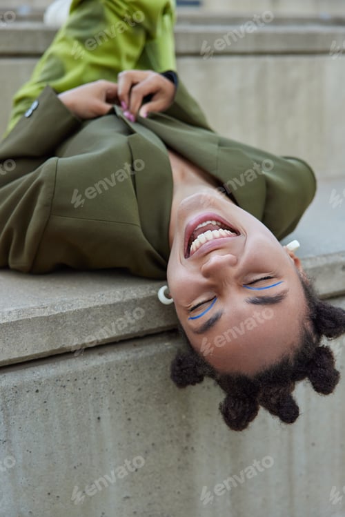 Preview: Overjoyed Fashionable Young Woman With Trendy Hairstyle Lies Outside Dressed In Green Stylish