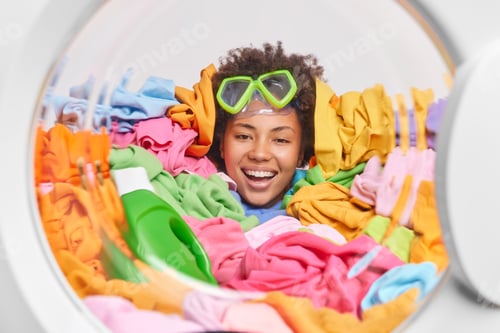 Vista previa: Positive Dark Skinned Woman With Curly Hair Wears Snorkeling Mask Drowned In Multicolored Laundry