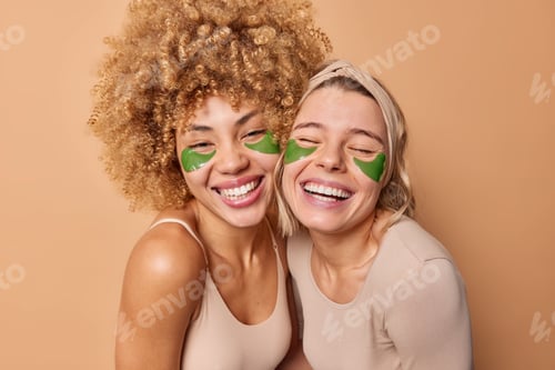 Preview: Positive Young Female Friends Smile Broadly Have Fun Together Apply Green Hydrogel Patches Under