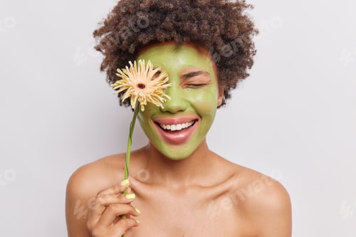 Preview: Skin Care And Beauty Concept. Positive Curly Haired Woman Applies Green Nourishing Mask Holds