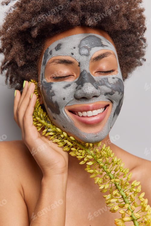 Preview: Close Up Shot Of Curly Haired Young Woman Applies Natural Homemade Clay Herbal Facial Mask Keeps