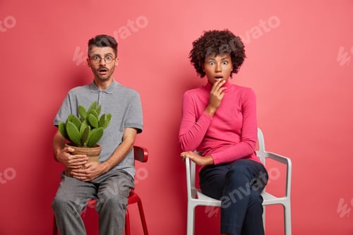 Preview: Shocked Diverse Young Woman And Man Keep Distance Sit On Chairs Stares Surprised Find Out