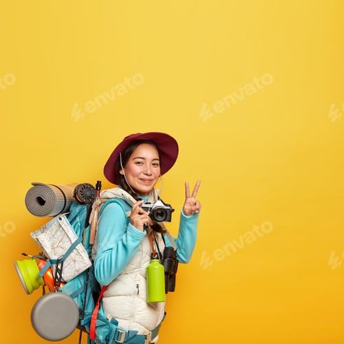 Preview: Vertical Image Of Active Female Traveler Makes Peace Gesture, Holds Retro Camera For Taking Pics