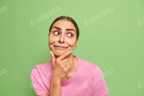 Preview: Portrait Of Pensive Young Brunette European Woman Holds Chin And Looks Away Considers Something And