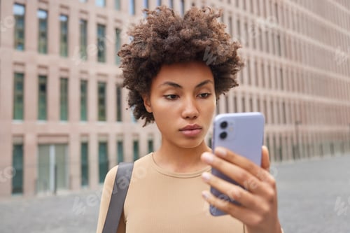 Preview: Young Attentive Curly Sportswoman Concentrated At Smartphone Screen Watches Video Of Sport Training