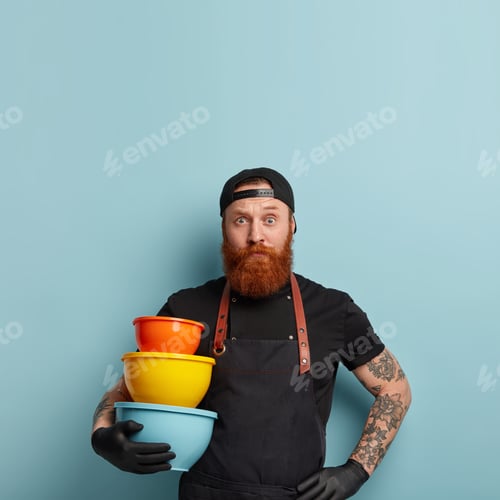 Preview: Vertical Shot Of Puzzled Bearded Male Works In Culinary Sphere, Carries Empty Kitchen Utensils