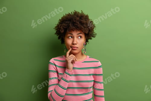 Preview: Horizontal Shot Of Good Looking Curly Woman Ponders On Something And Concentrated Thoughtfully