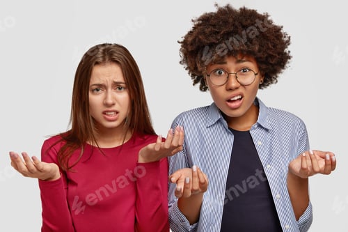 Preview: Photo Of Clueless Two Young Multiethnic Women With Uncertain Displeased Looks, Frown Faces, Spread