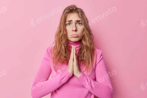 Preview: Upset Good Looking Young Woman With Needy Face Begs For Something Stands In Pray Pose Looks Sadly