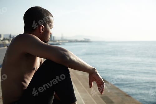 Preview: Handosme Dark-Skinned Sportsman With Muscular Athlete Body Sitting On Sidewalks At Ocean, Watching