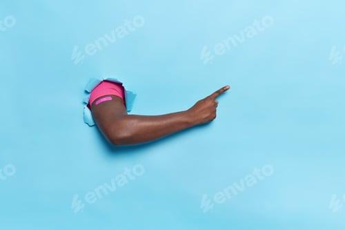 Preview: Unrecognizable Man With Dark Skin Breaks Through Blue Paper Background Wears Adhesive Plaster After