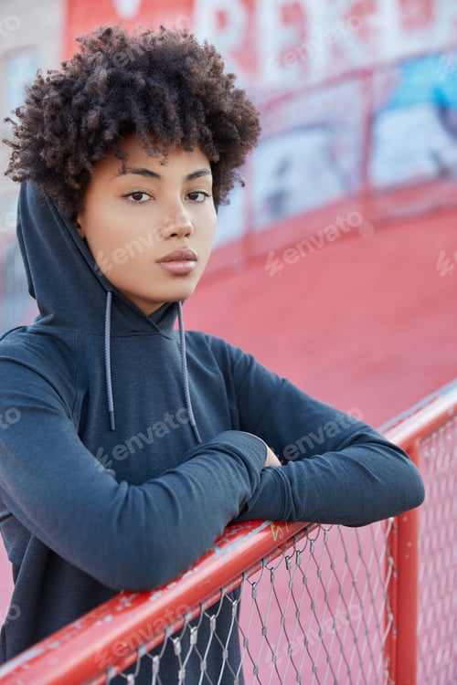 Preview: Vertical Shot Of Serious Sportswoman Has Outdoor Training In Playground, Dressed In Hoodie, Leans